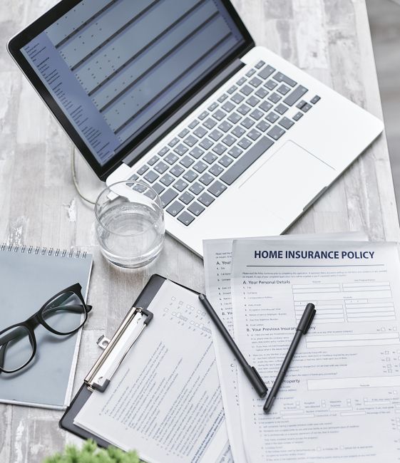 A person dressed in formal business attire, including a dark suit and white shirt, holding a clipboard with a home insurance policy form attached. The individual is gripping the clipboard with their left hand, which is partially visible, while the right hand rests against their body. The form on the clipboard features printed text, blank fields for personal details, and checkboxes, and is titled 'Home Insurance Policy.' The background appears slightly blurred, suggesting an indoor environment, possibly an office or a setting related to house removals or relocation services. This image relates to the process of home relocating and the importance of insurance and liability coverage, as referenced on the page about insurance and liability for Rotherhithe removals at manwithavanrotherhithe.co.uk, emphasizing the significance of proper documentation and protection during a move.